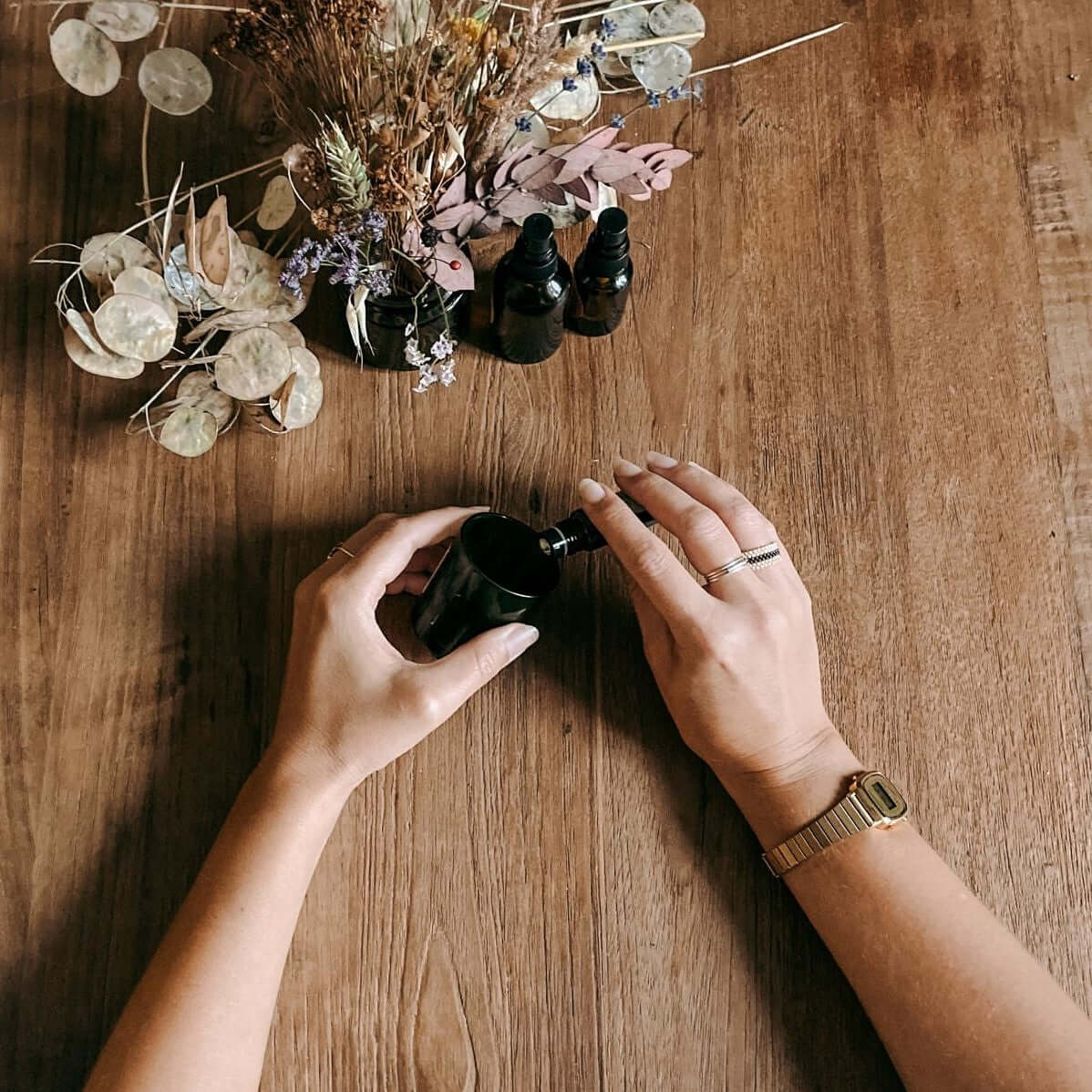 Zwei Hände befüllen kleine Flasche mit Flüssigkeit, Blumen im Hintergrund – naturkosmetik workshop, ätherische öle, diy parfum, auch für Firmenevents.