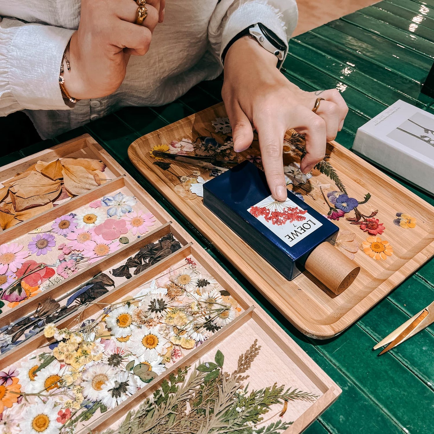 Parfum wird mit Trockenblumen verziert, daneben Schälchen mit verschiedenen Blüten im Workshop von GRIMMS GARTEN Berlin