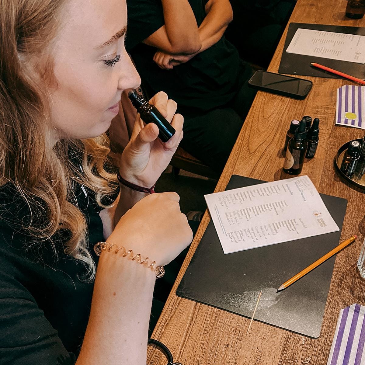 Frau riecht an eigenem Parfum mit Zettel und Materialien auf Tisch – parfum selber machen, aromatherapie, diy duftkurs, auch für Firmenevents.