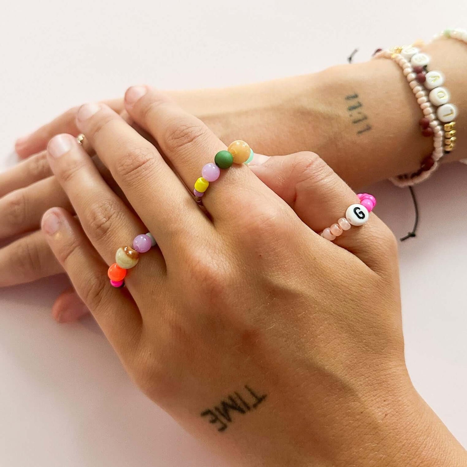 Zwei Hände mit Ringen und Armbändern mit Buchstaben – DIY Perlenschmuck Workshop, individuelle Accessoires.