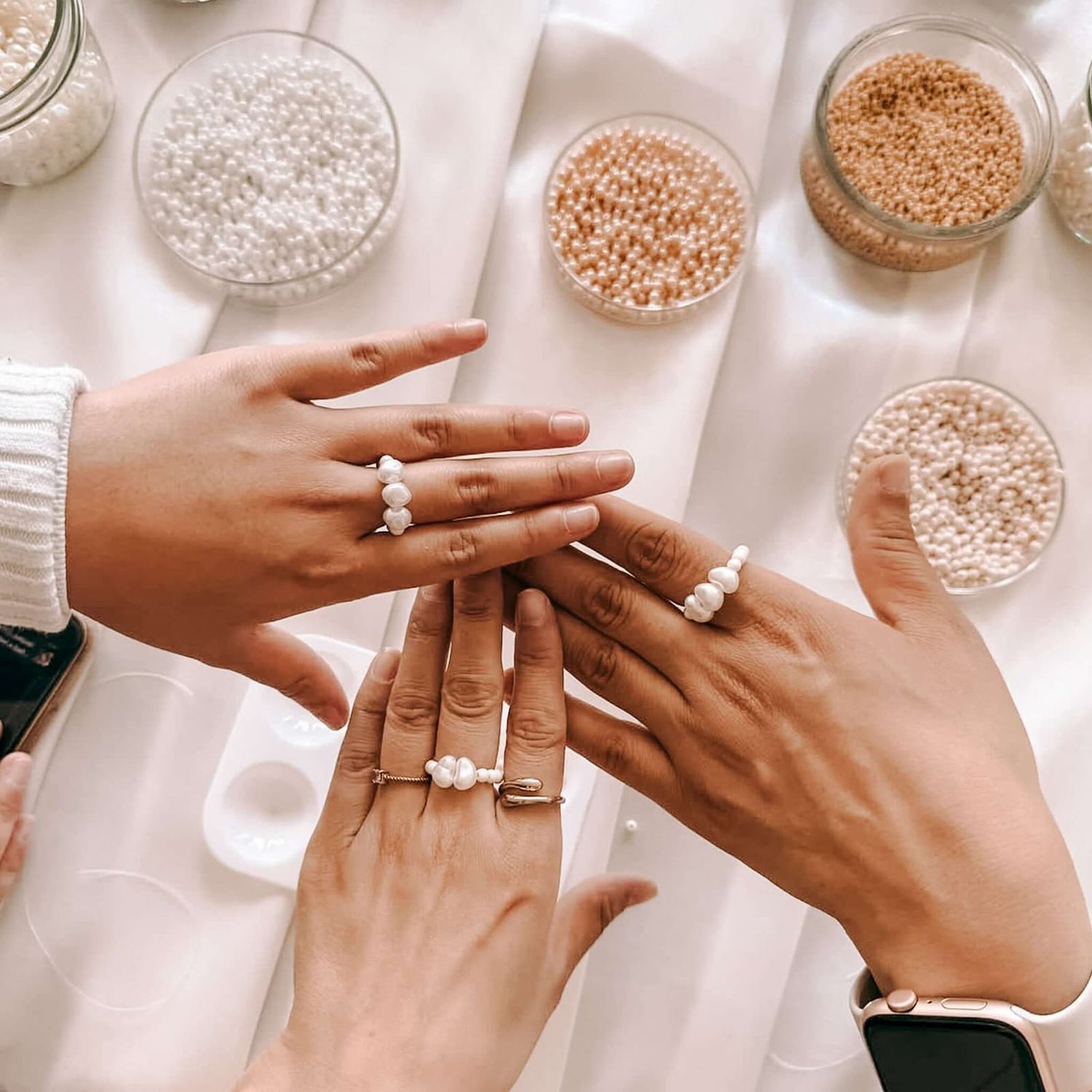 Drei Hände mit Perlenringen, Gläser mit Perlen im Hintergrund – DIY Perlenschmuck, Perlenringe gestalten.