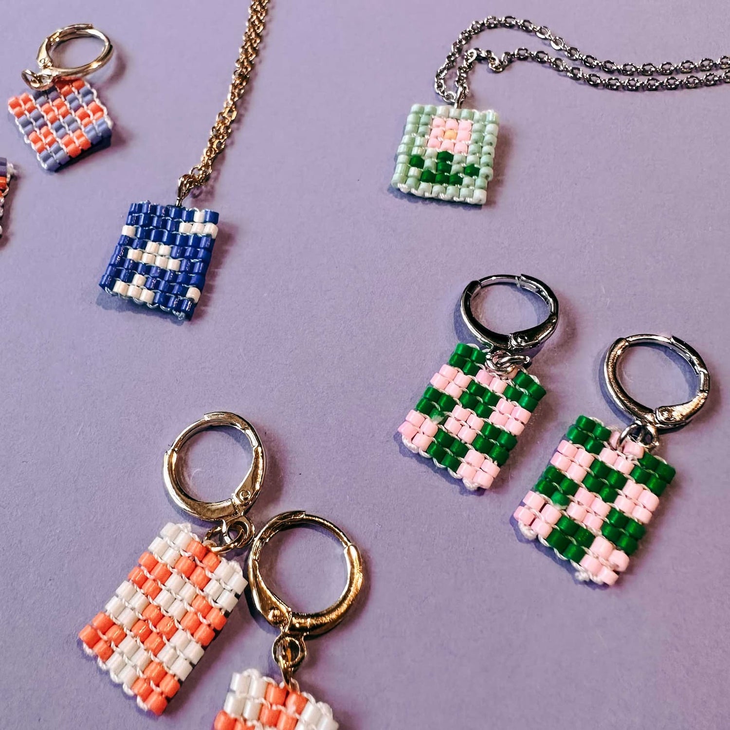 Mehrere fertige Perlenohrringe und zwei bunte Halsketten mit verschiedenen Mustern auf lila Hintergrund beim DIY Perlenschmuck Workshop von GRIMMS GARTEN in Berlin