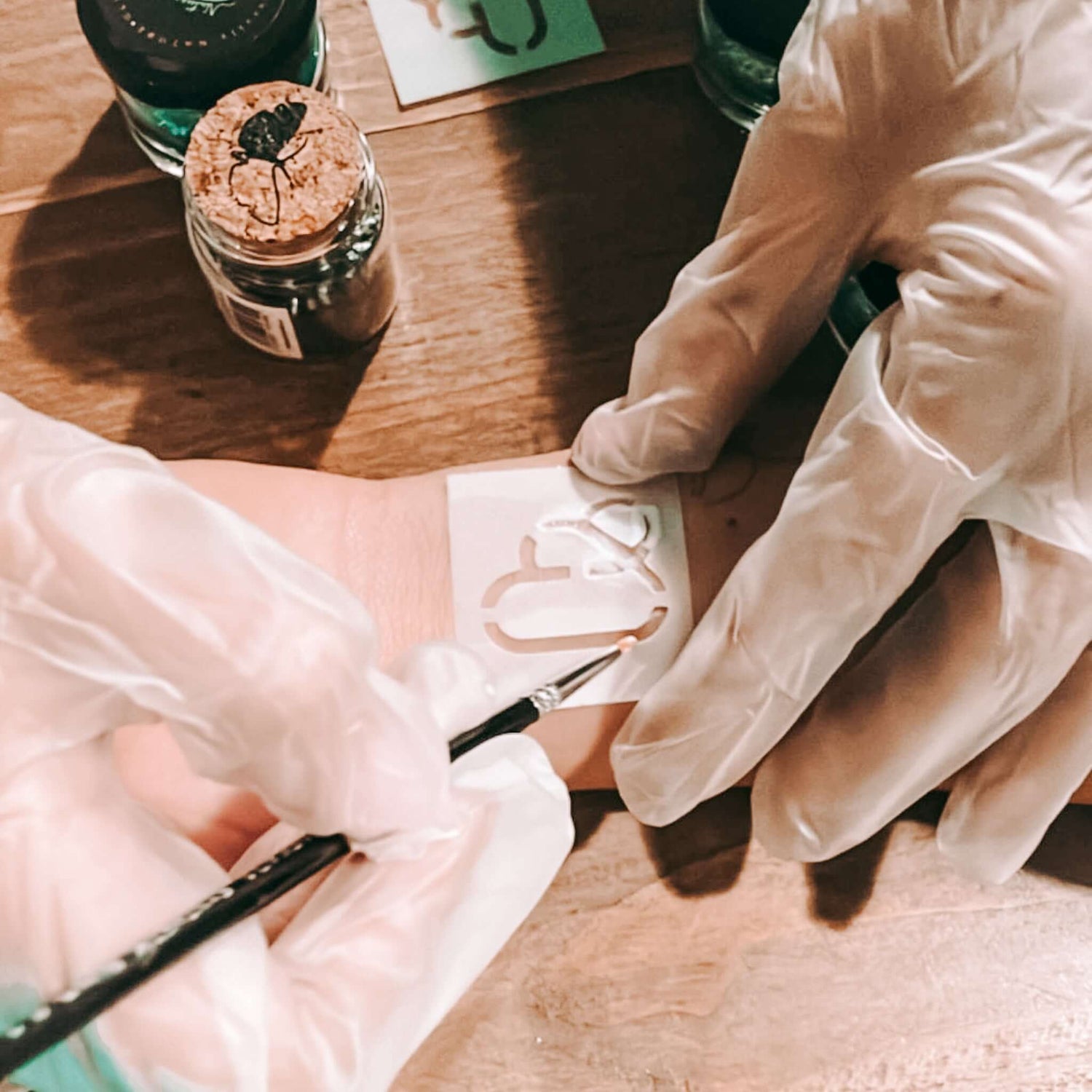 Zwei Hände malen Logo auf Arm mit Pinsel und Schablone – Bio-Glitzertattoos für Firmenevent.