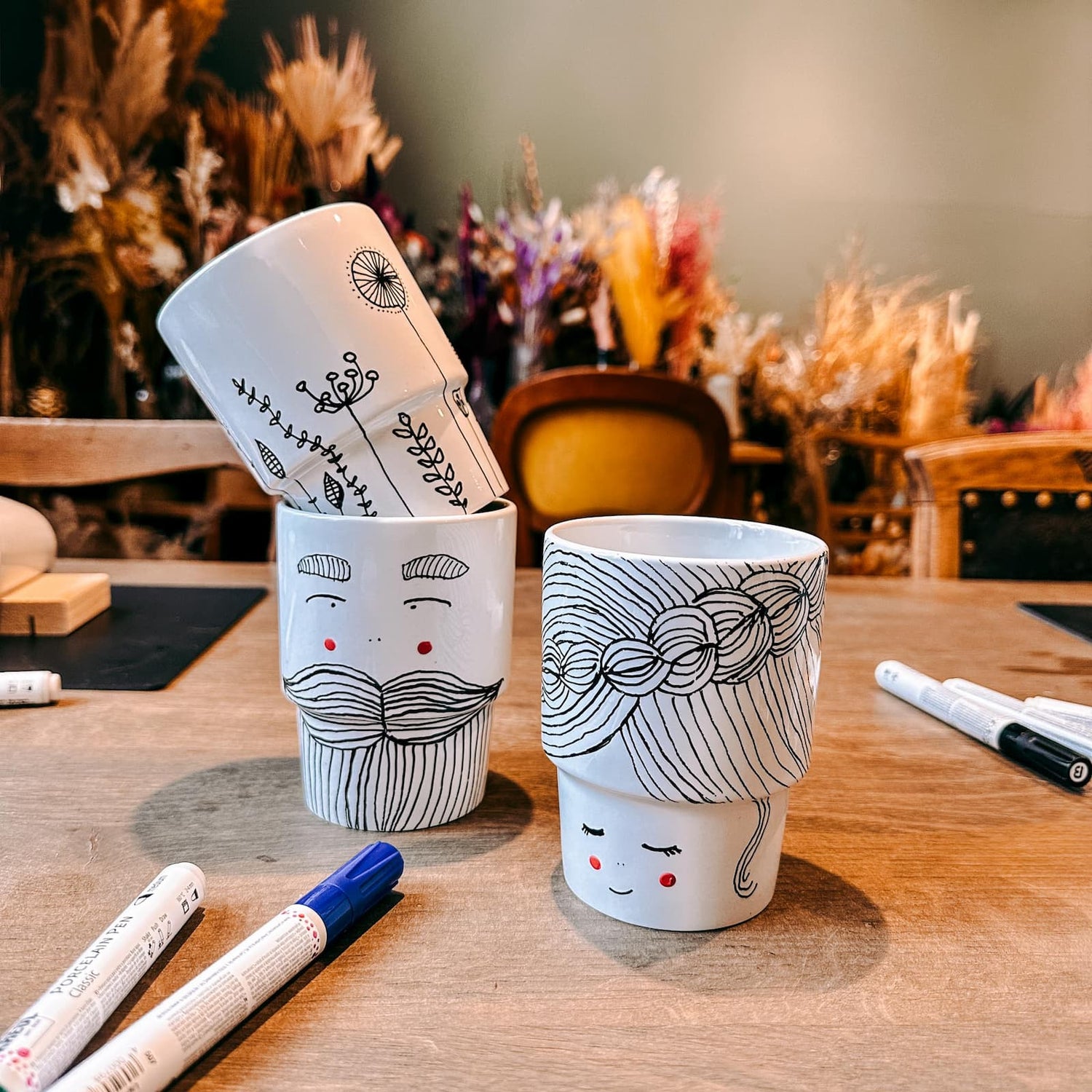 Drei Keramik To-Go Becher mit Motiven – Paar mit Frau, Mann und Blumenwiese – beim Keramik bemalen Workshop von GRIMMS GARTEN, Kreativkurs in Berli