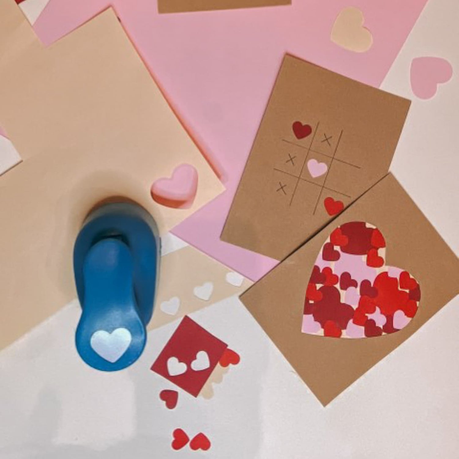 Herzstanzer neben Papier mit ausgestanzten Formen und zwei braunen Postkarten mit roten und rosa Herzmotiven beim kreativen Postkarten Workshop von GRIMMS GARTEN in Berlin