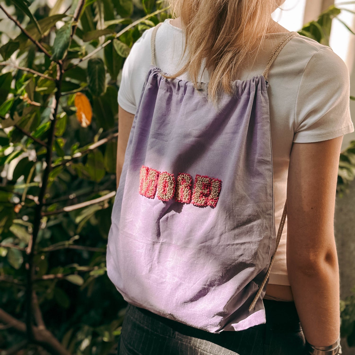 Person trägt lilanen Jutebeutel mit gepunchtem Spruch – Punch-Needle Workshop Berlin.