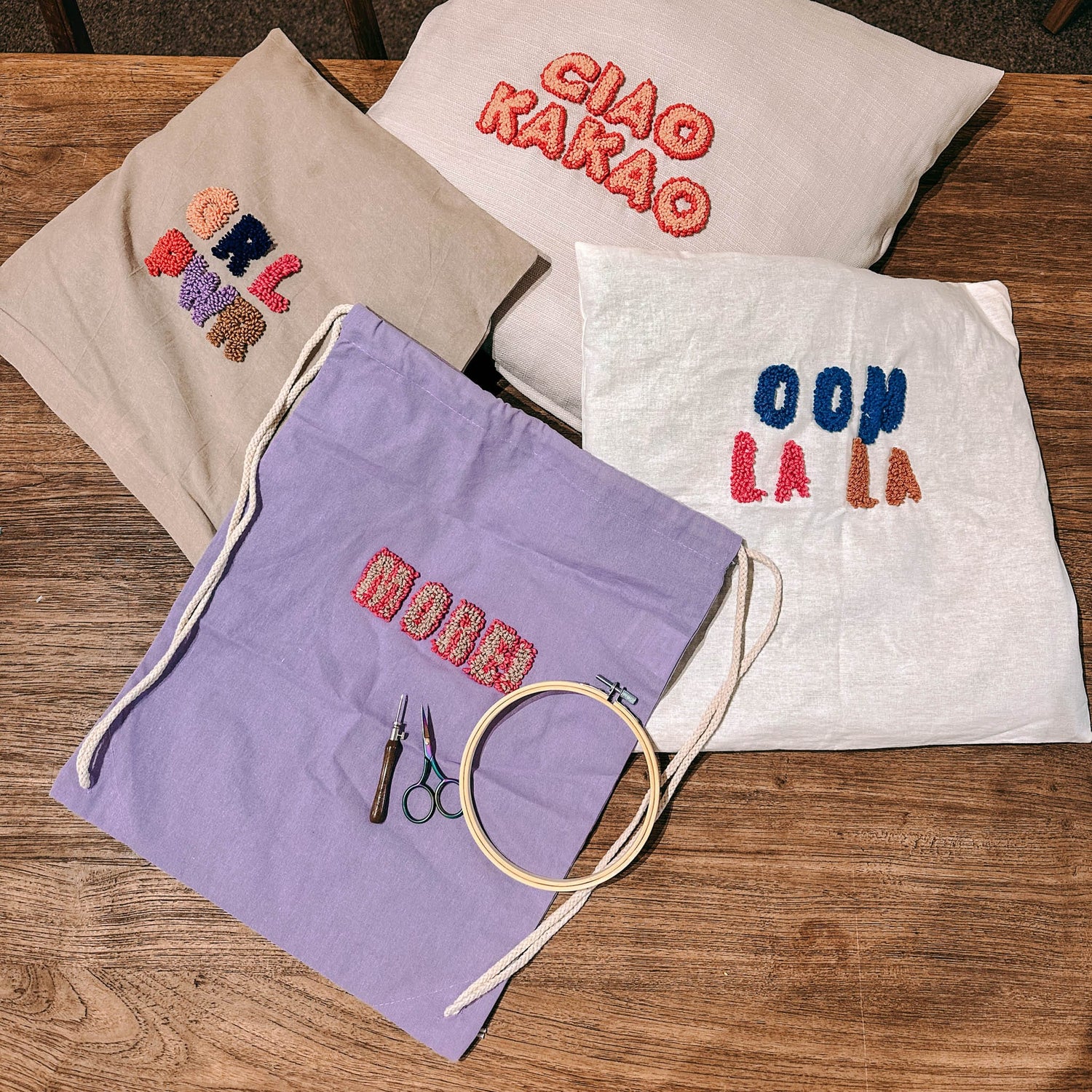 Verschiedene Stoffe mit Sprüchen, Materialien und Wolle auf Tisch – Punch-Needle Workshop Berlin.