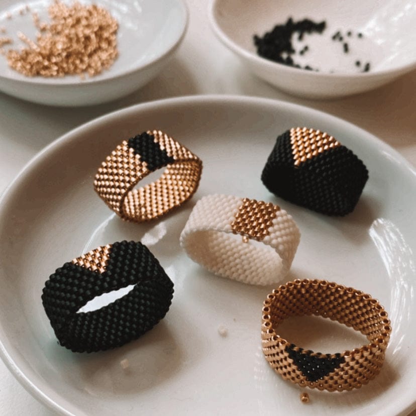 Nahaufnahme von fünf fertigen Ringen aus goldenen, schwarzen und weißen Miyuki Perlen – DIY Perlenring Workshop