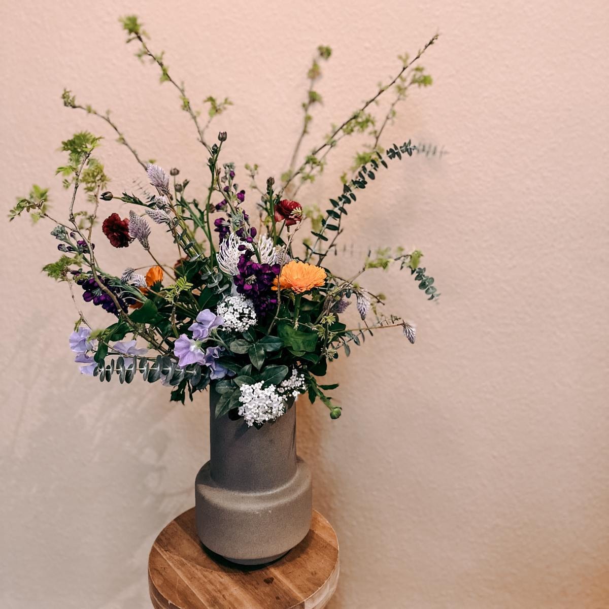 Bunter Blumenstrauß in Vase auf Holzhocker – Workshop für individuelle Sträuße, auch als Teamevent buchbar.