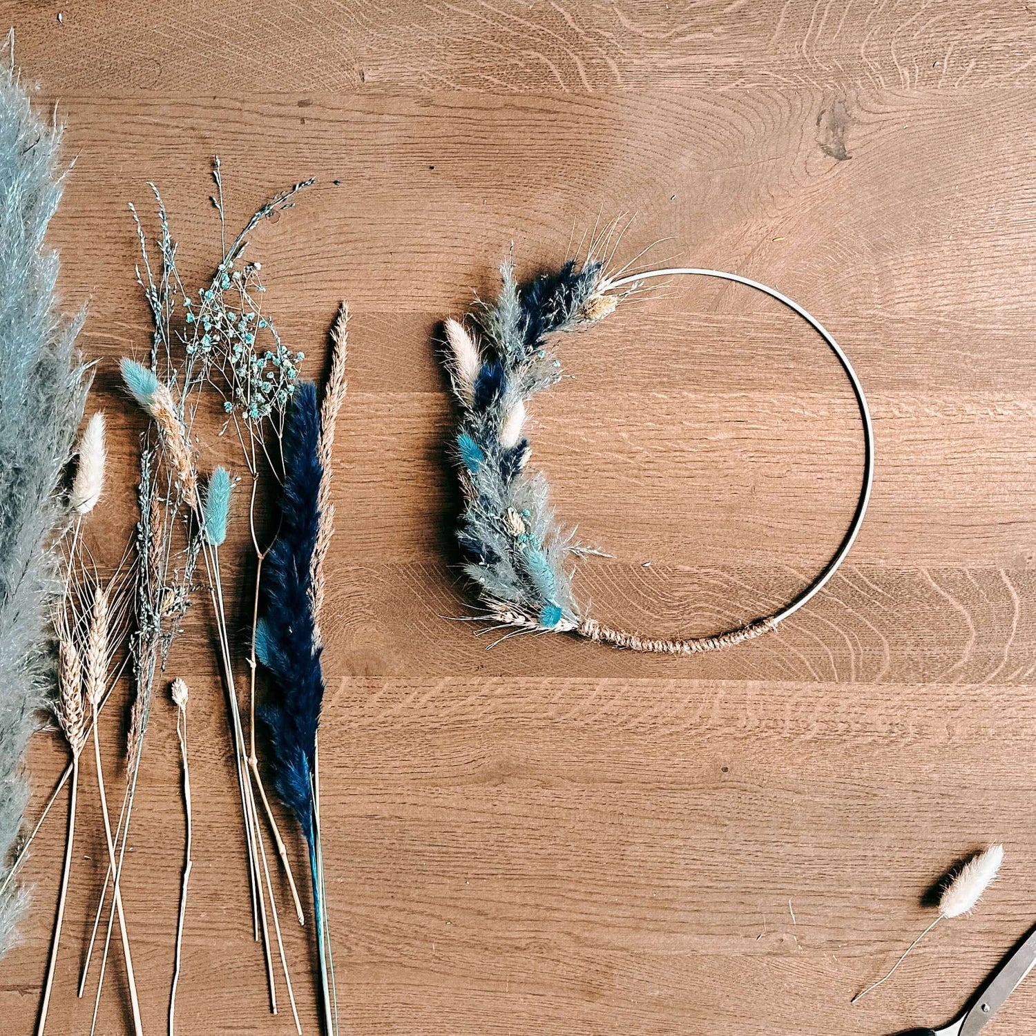 Fertiger blauer Blumenring auf Tisch mit weiteren Trockenblumen daneben – DIY Bastelset.