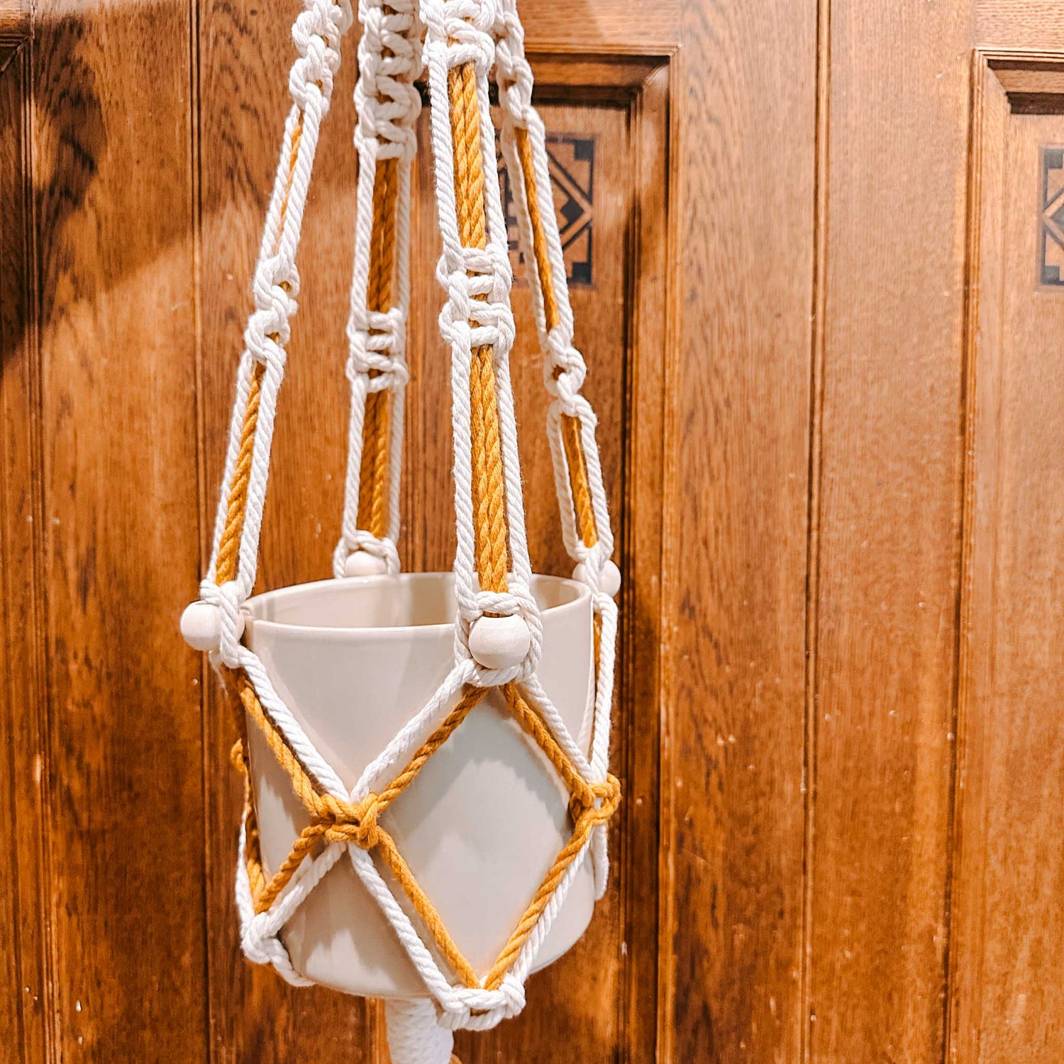 Makrameeampel in Weiß-Braun mit Blumentopf vor Holzwand – DIY Makramee Workshop, Vintage Deko, Boho Stil.