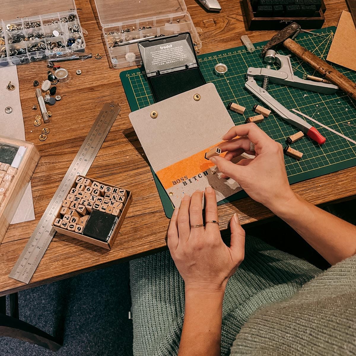 Hände stempeln „Boss Bitch“ auf oranges Leder-Etui, kreativer DIY Workshop bei Grimms Garten Berlin