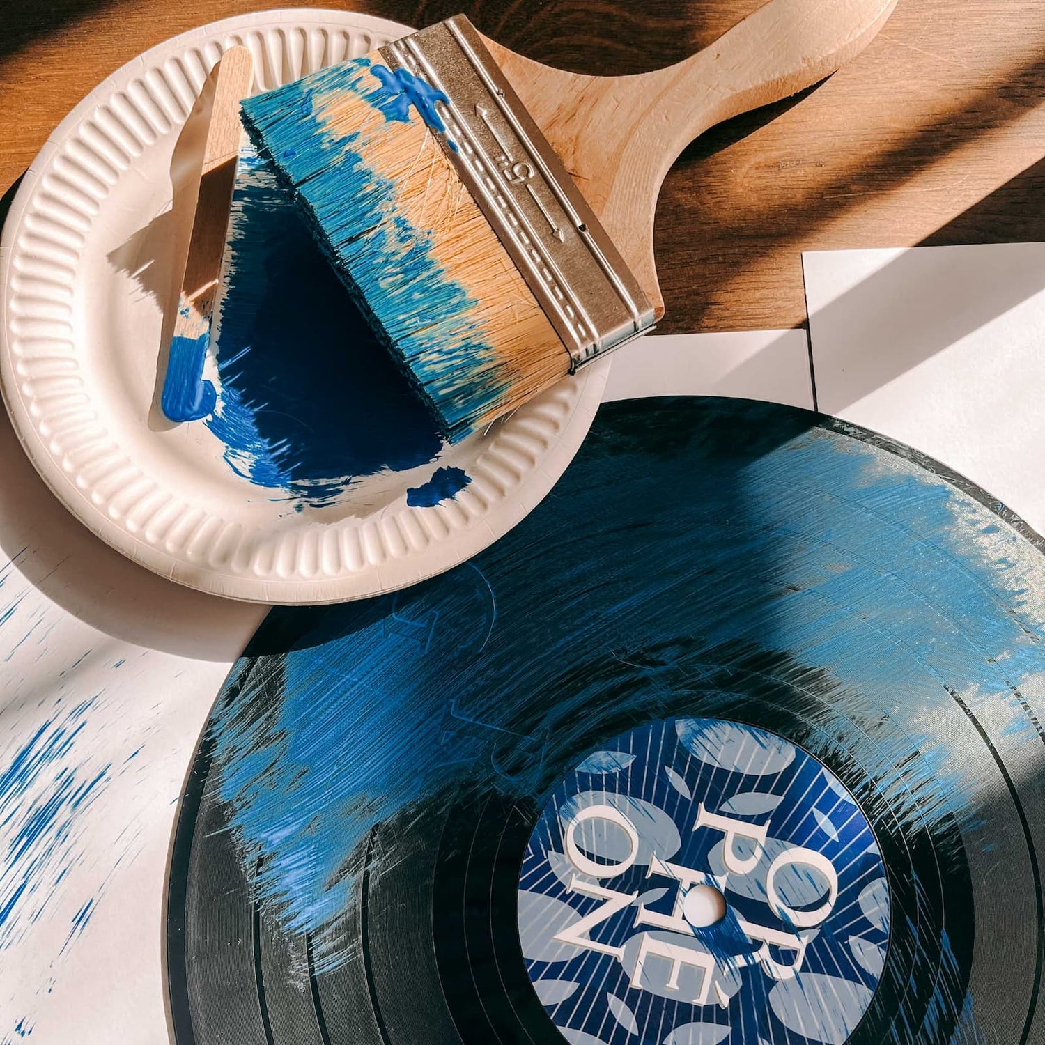 Schallplatte wird mit blauer Farbe und Pinseln bemalt beim Vinylplatten bemalen Workshop von GRIMMS GARTEN, DIY Kreativkurs in Berlin