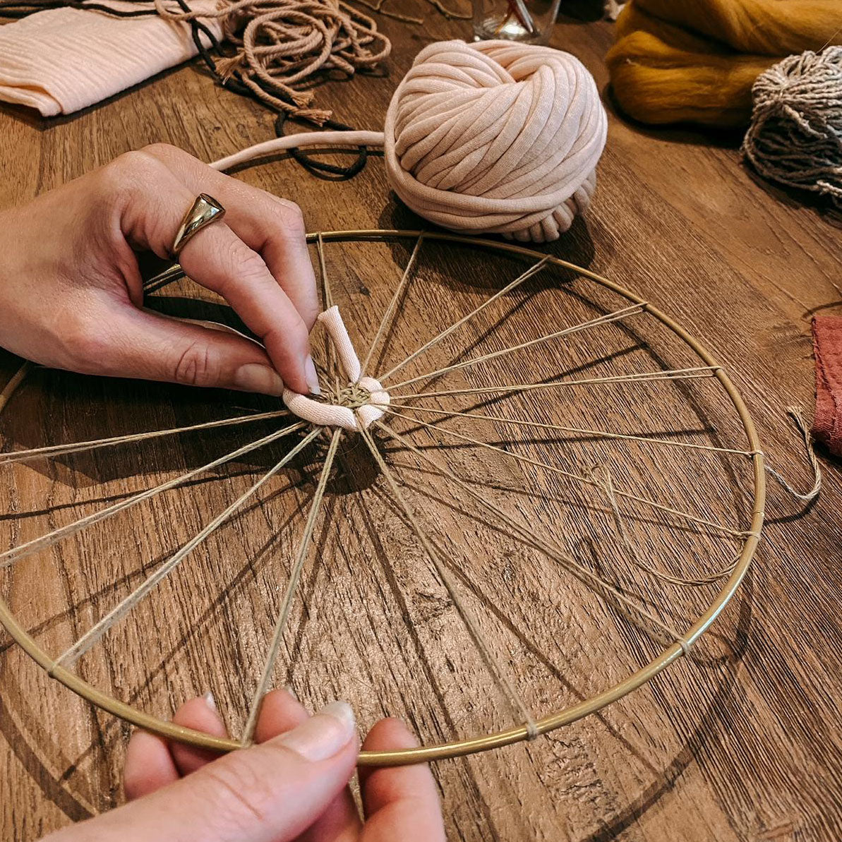 Hand webt weiße Wolle auf Rundweben – Workshop für kreative Wandbilder im Boho Stil.