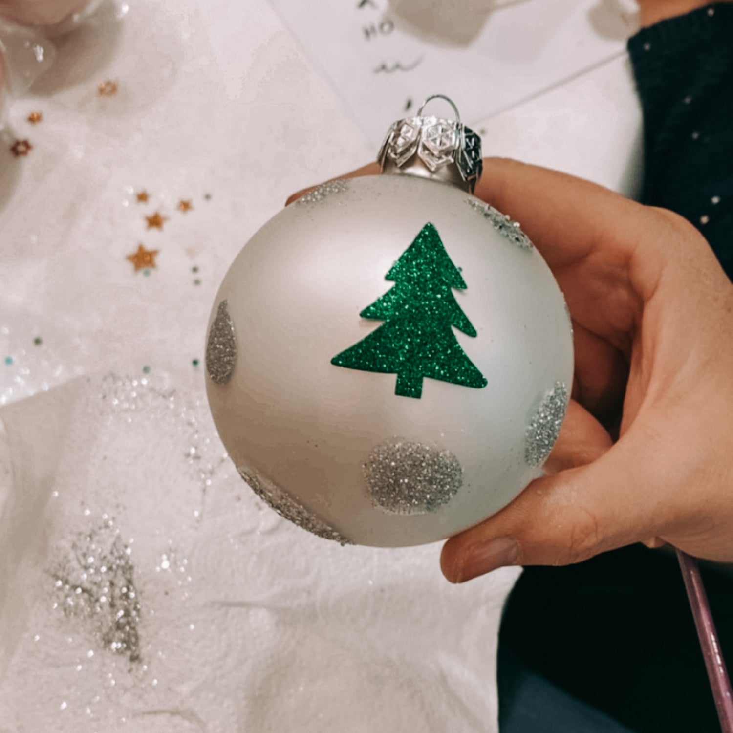Hand hält Kugel mit grünem Tannenbaum und silbernen Kugeln – Weihnachtskugeln bemalen.