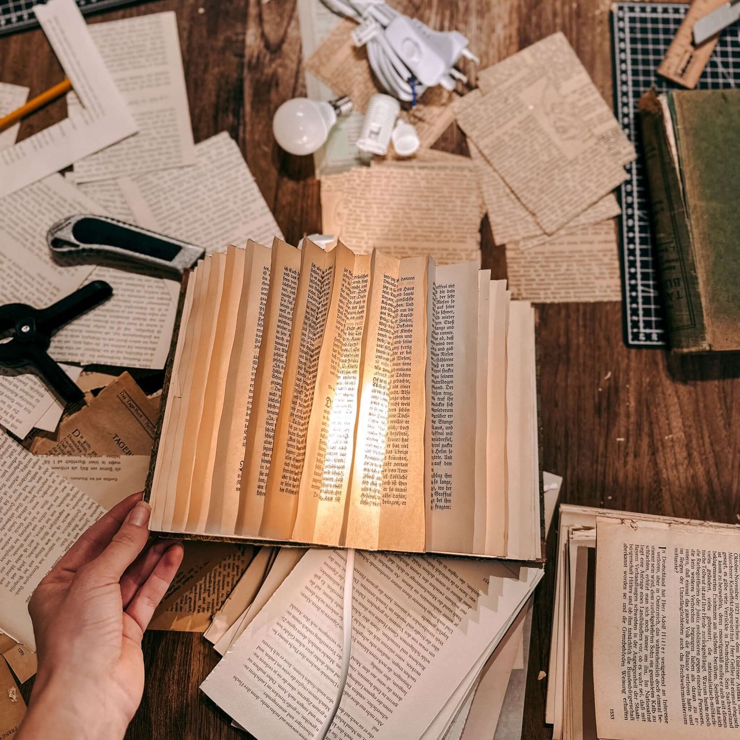 Hand hält leuchtende Buchlampe, Buchseiten im Hintergrund – buchlampe, upcycling workshop, nachhaltige kunst. Auch für Firmenevents.