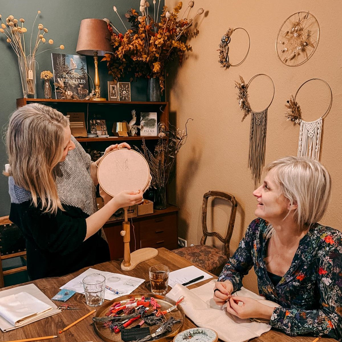 Frau zeigt anderer Frau Stickrahmen, Materialien auf Tisch – stick workshop, embroidery kurs, handarbeit lernen, nachhaltige mode.