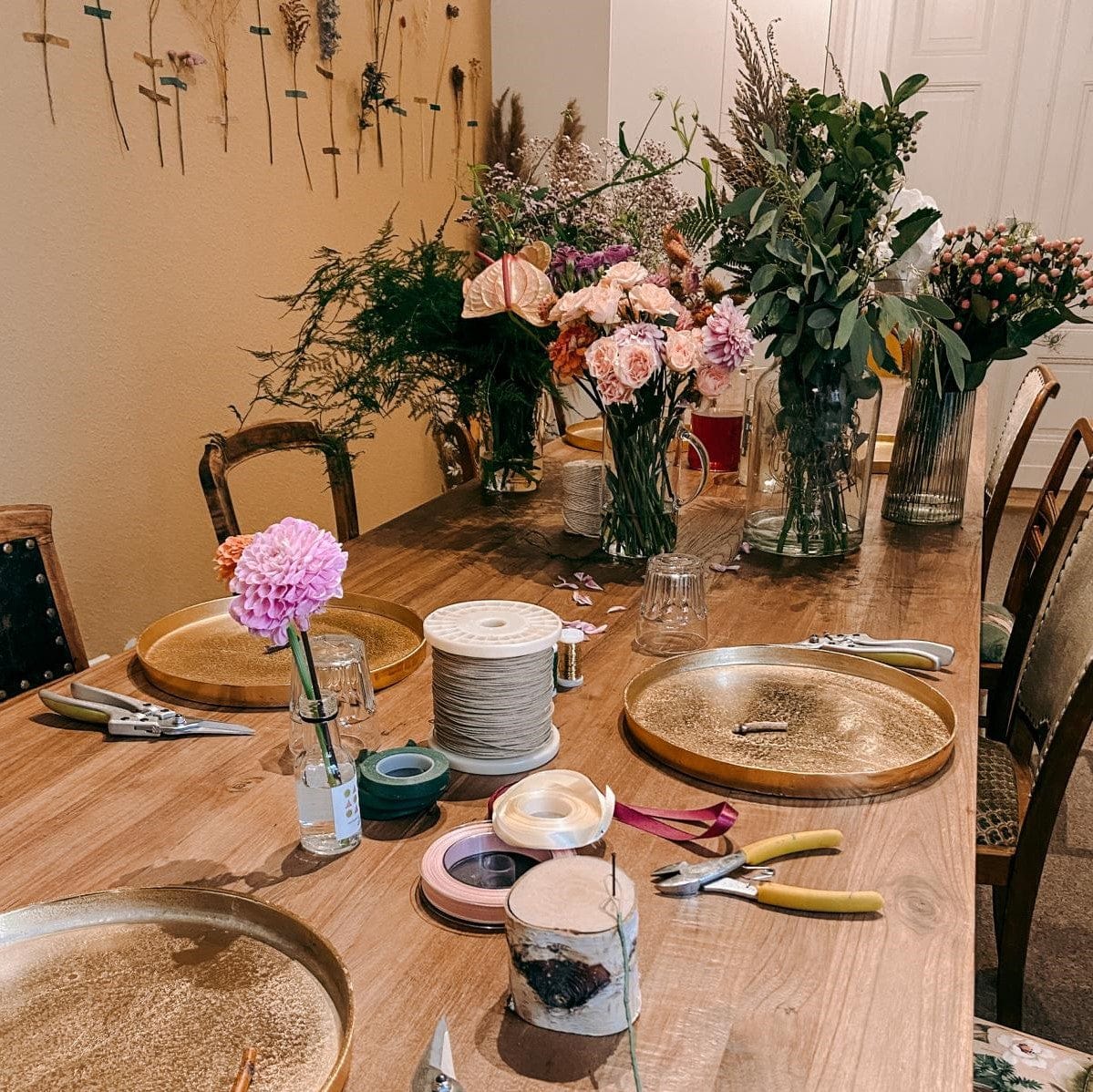 Blumensträuße in Vasen im Hintergrund, bunte Drähte und goldene Tabletts auf Tisch, DIY Workshop bei Grimms Garten Berlin