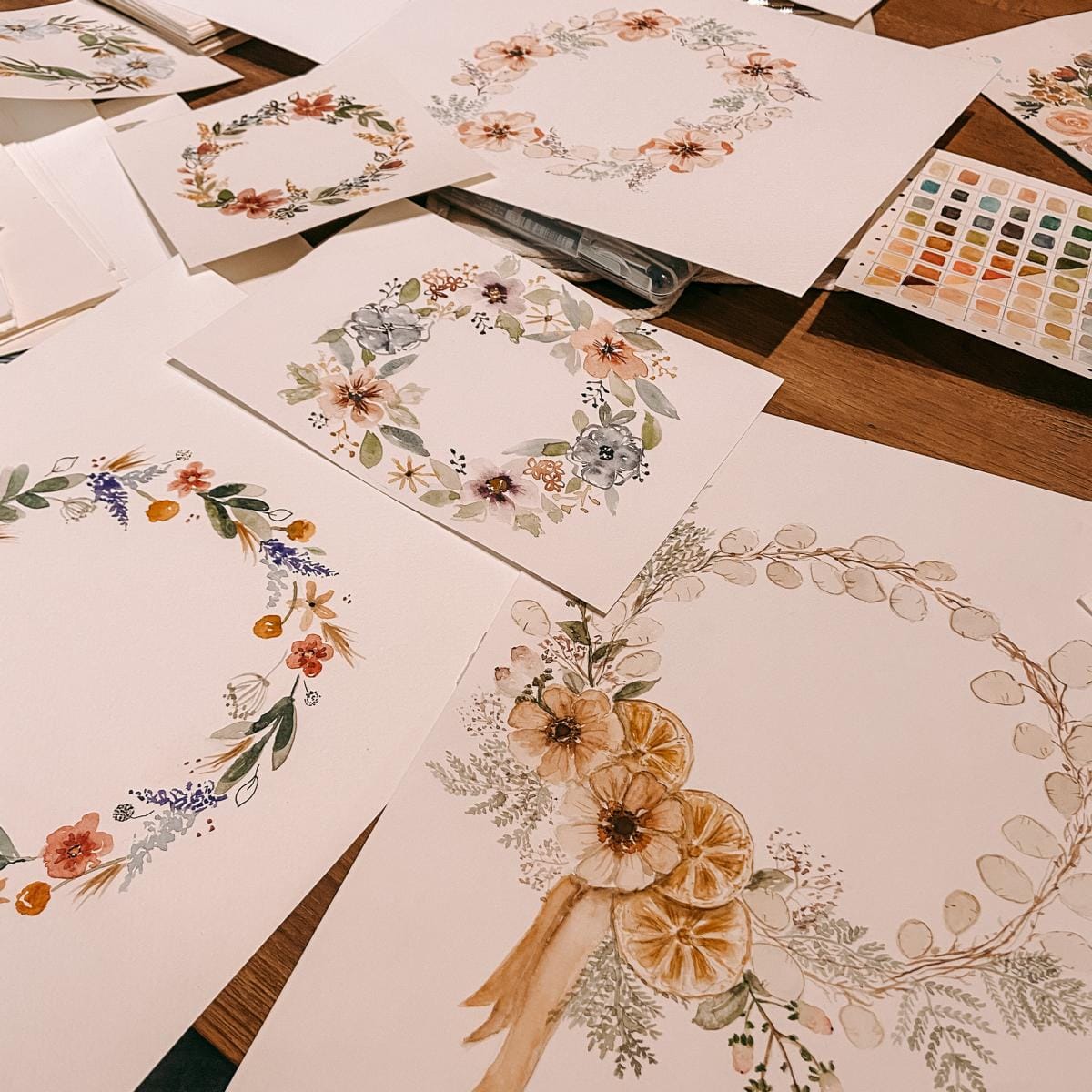 Verschiedene gemalte Aquarell-Blumenkränze auf Holztisch mit Pinseln – watercolor florals, kreativworkshop, aquarellkunst.