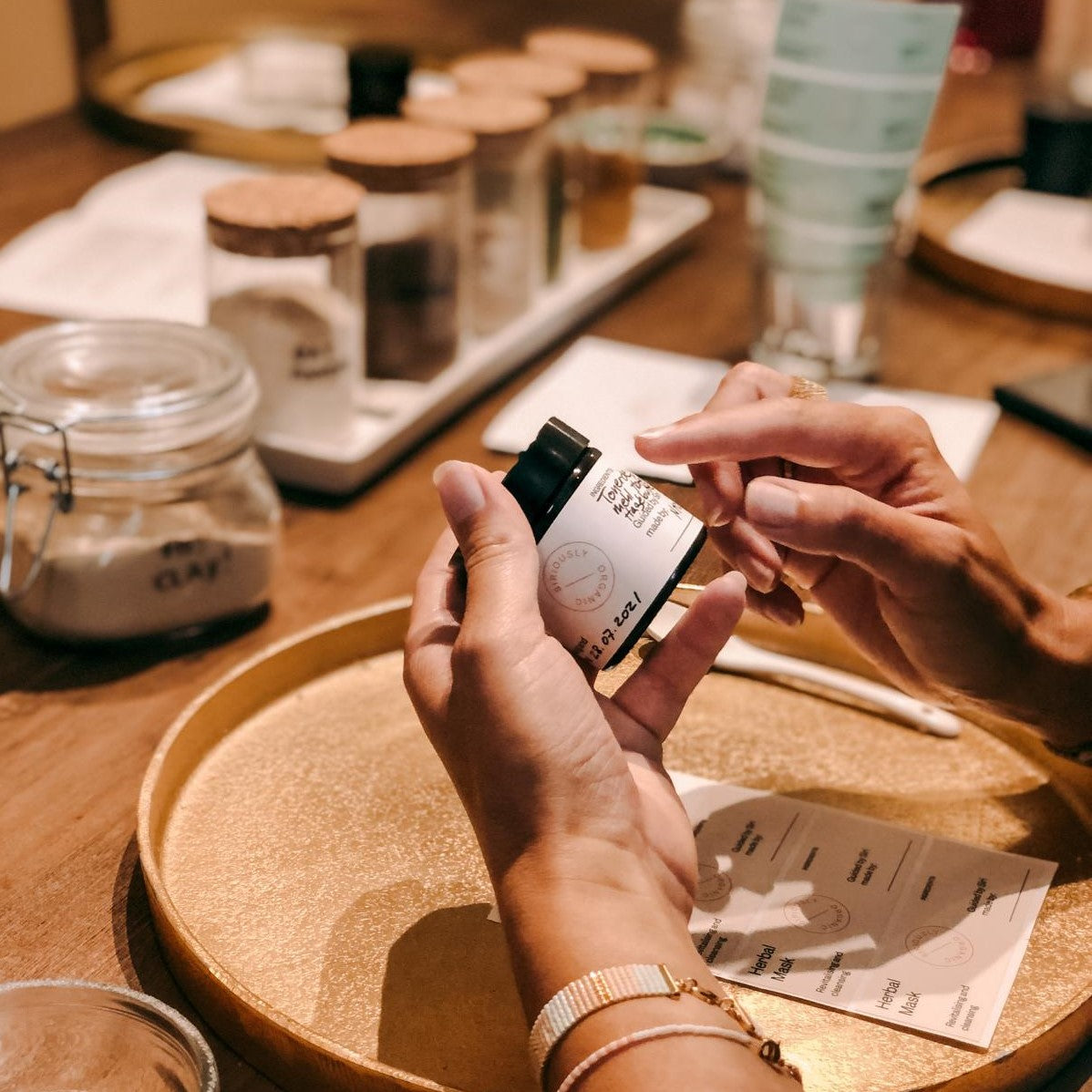 Zwei Hände halten Tube mit fertiger Maske über goldenem Tablett – DIY Hautpflege.