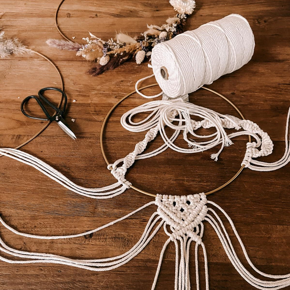 Makramee Ring mit Blumen und Garn auf Tisch – DIY Boho-Kunst im Workshop.