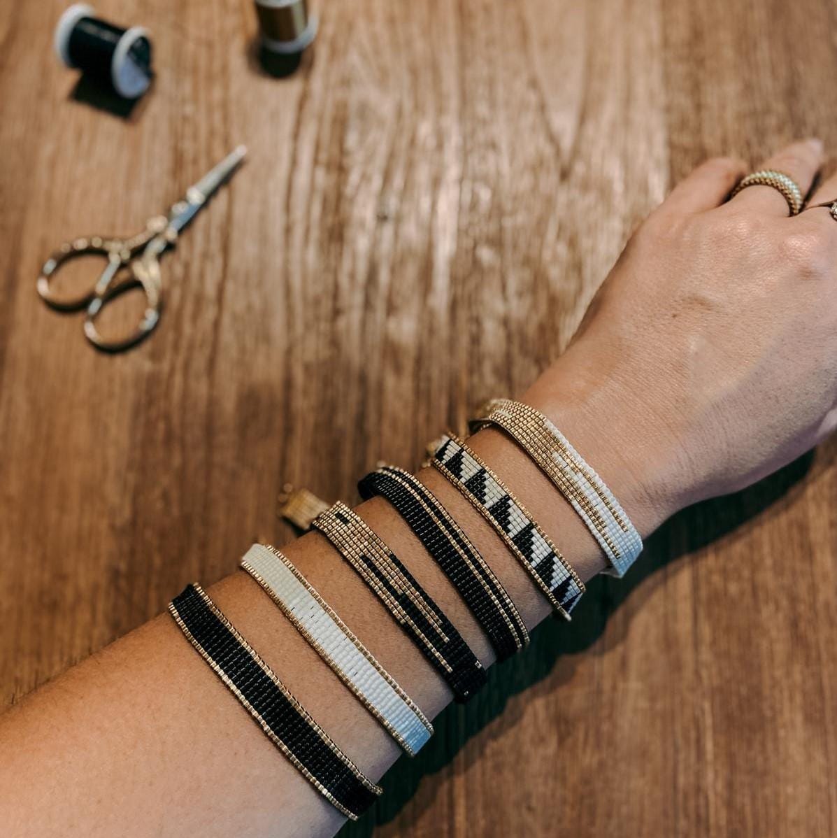 Arm mit sechs Miyuki Perlenarmbändern in Weiß, Gold und Schwarz – DIY Armband Workshop