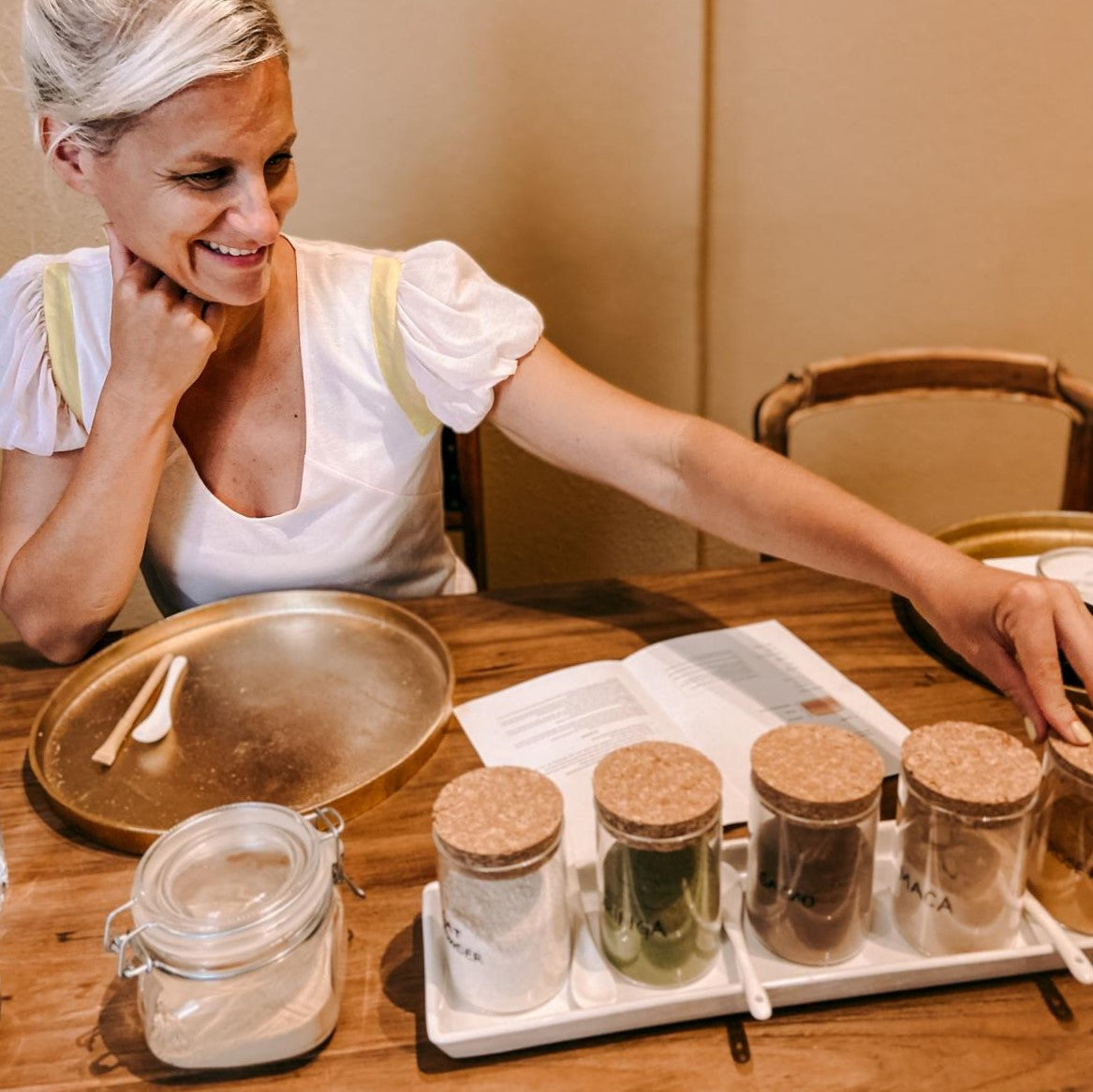 Frau betrachtet Gläser mit grünem, weißem und braunem Pulver – Hautpflege Workshop.