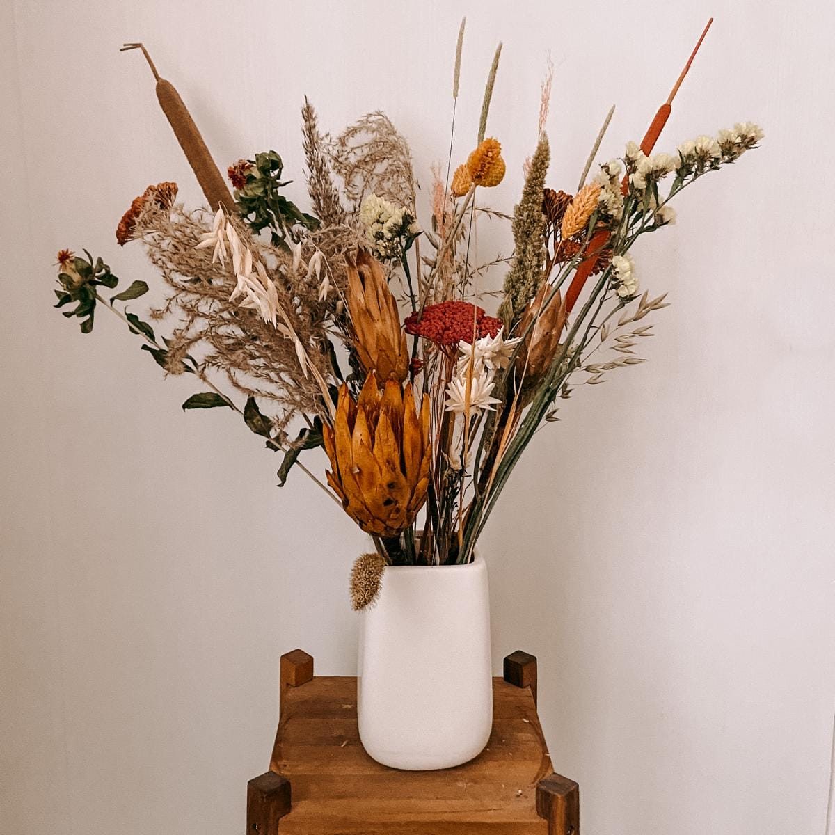 Trockenblumenstrauß Sonnenschein in weißer Vase, warme Rot- und Orangetöne, dekoratives Highlight für Zuhause.