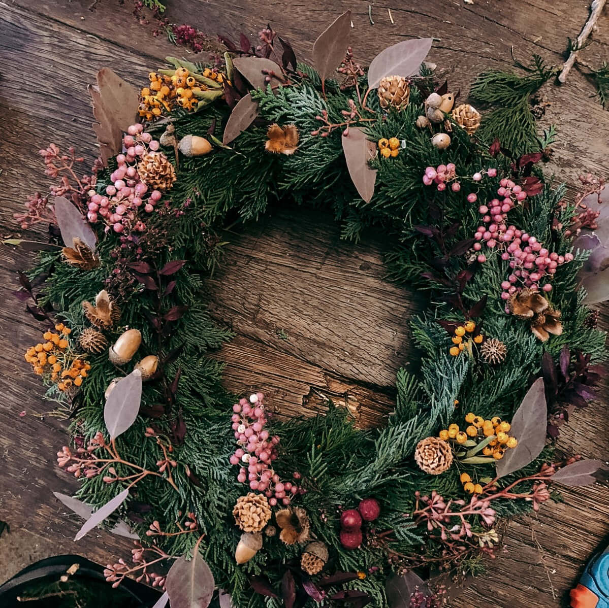 Bunter, fertiger Weihnachtskranz mit Tannenzweigen auf Tisch – weihnachtskranz tür, diy weihnachtsdeko, auch für Firmenevents.