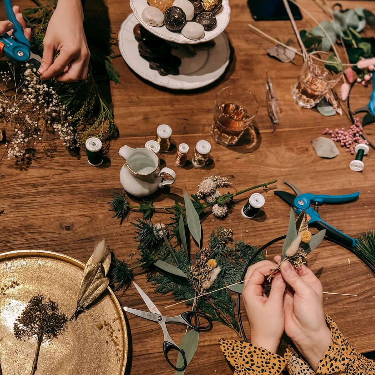 Tisch mit allen Materialien und zwei Händen beim Binden eines Rings – weihnachtsdeko ring, weihnachtskranz modern.
