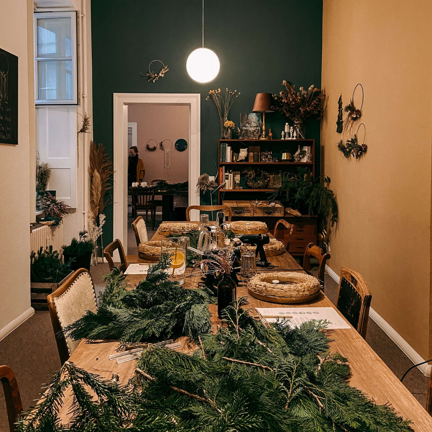 Tisch mit Materialien zum Kranzbinden, Raum mit fertigen Kränzen im Hintergrund – weihnachtsworkshop berlin, auch für Firmenevents.