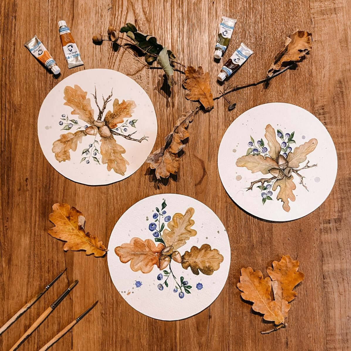 Drei fertige Aquarellbilder mit Zweigen und Farbtuben auf Tisch – Herbstmotive für Anfänger.