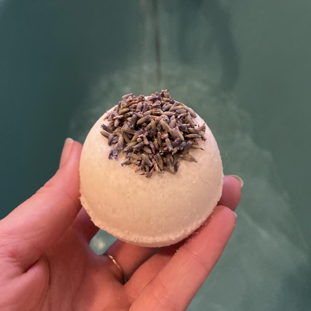 Hand hält vegane Badekugel „Lavendeltraum“ mit ätherischem Lavendelöl für entspannende Pflege.