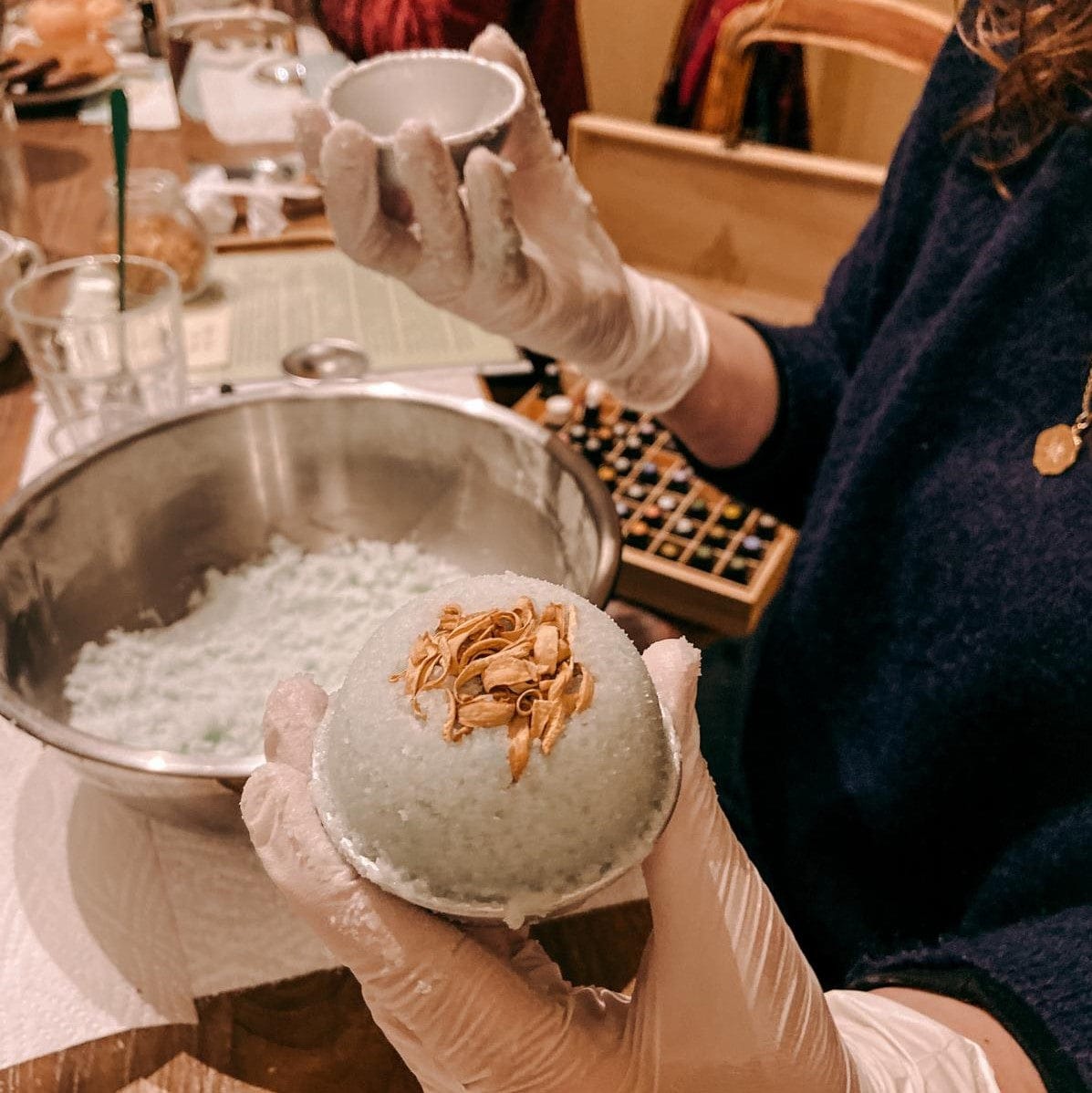 Eine Badekugel wird geformt, Kugel in Hand, Schüssel mit Material darunter – Badekugel, DIY Workshop, Aromatherapie.