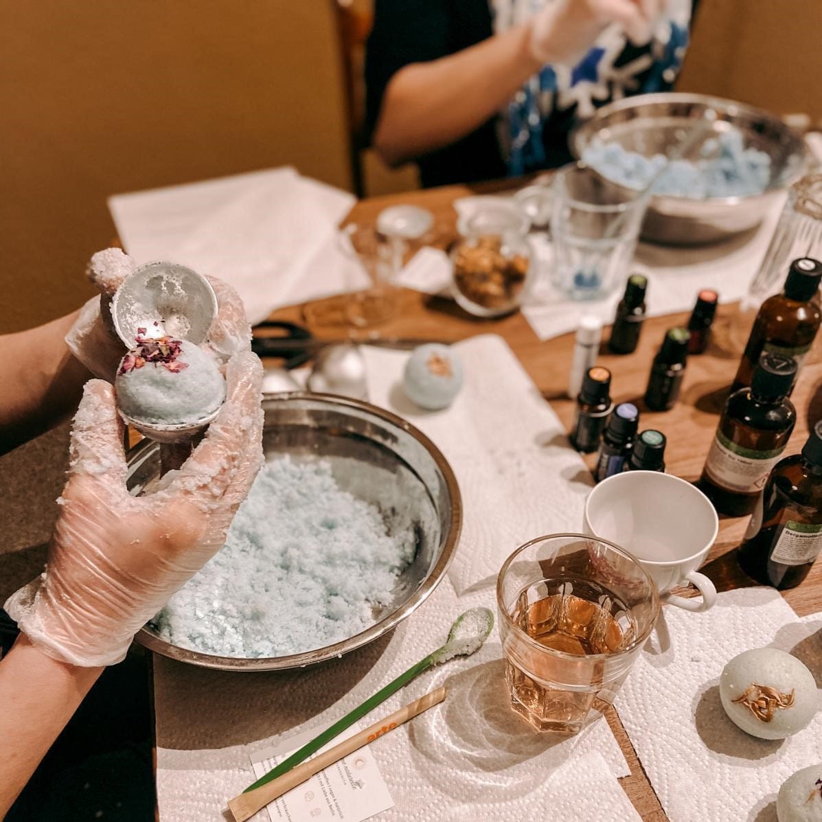 Zwei Stationen mit Materialien und Teilnehmerinnen, Badekugeln werden geformt – Badekugel, DIY Badekugel.