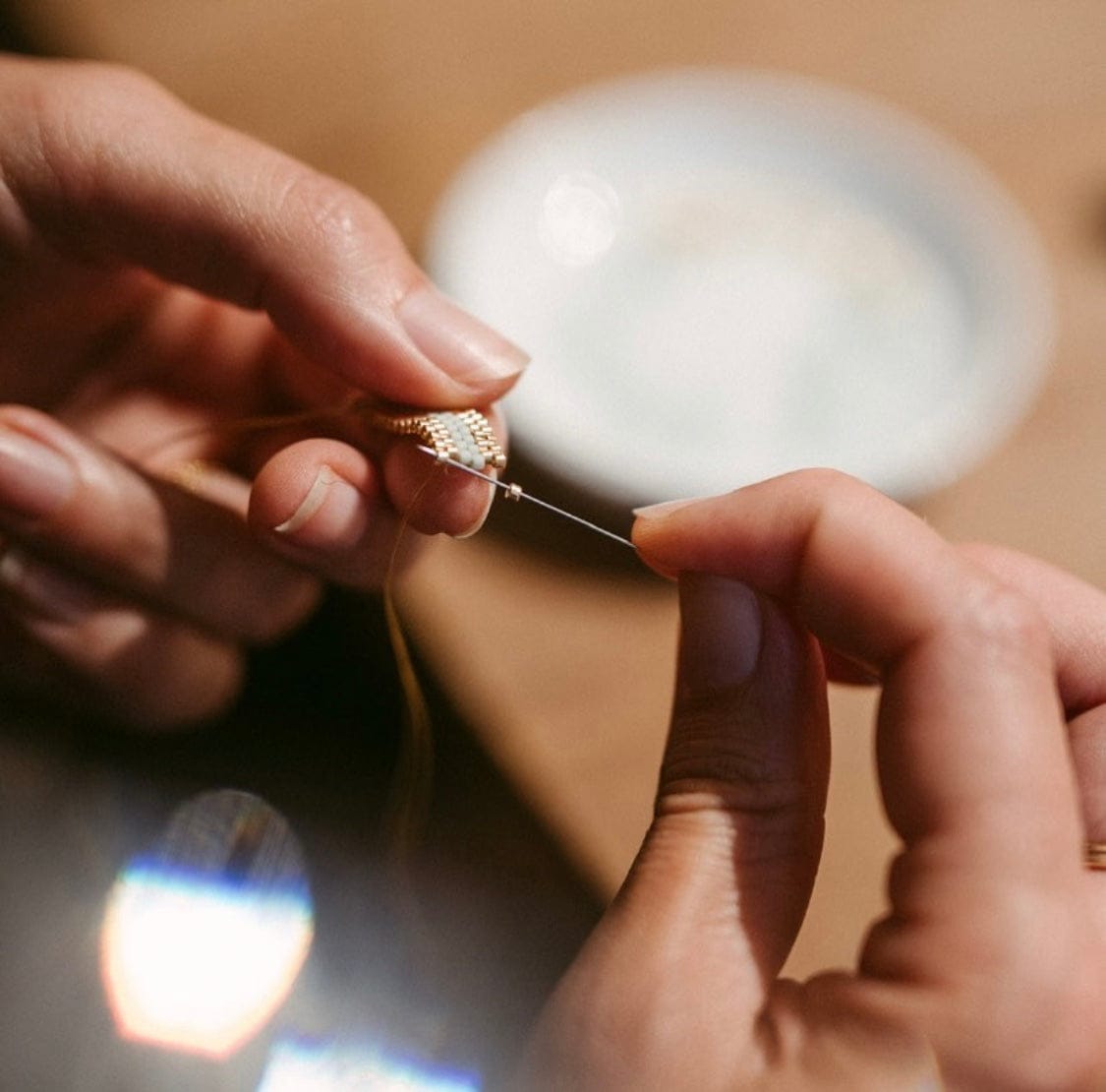 Zwei Hände fädeln weiße Perlen auf Draht, Nahaufnahme – DIY Perlenring, japanische Glasperlen