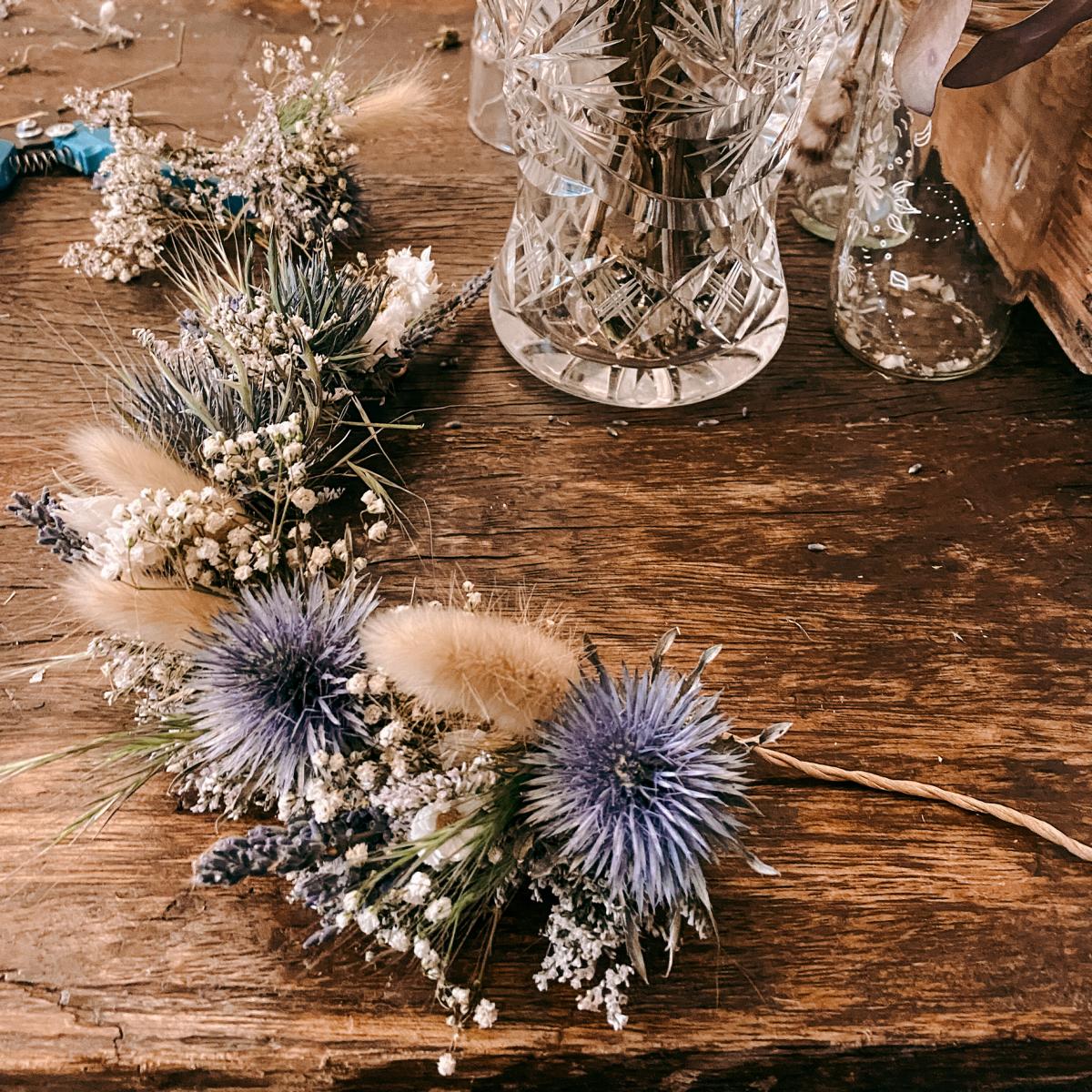 Halbfertige Blumenkrone mit blauen Akzenten auf Tisch – flower crown selber machen, diy blumenkranz