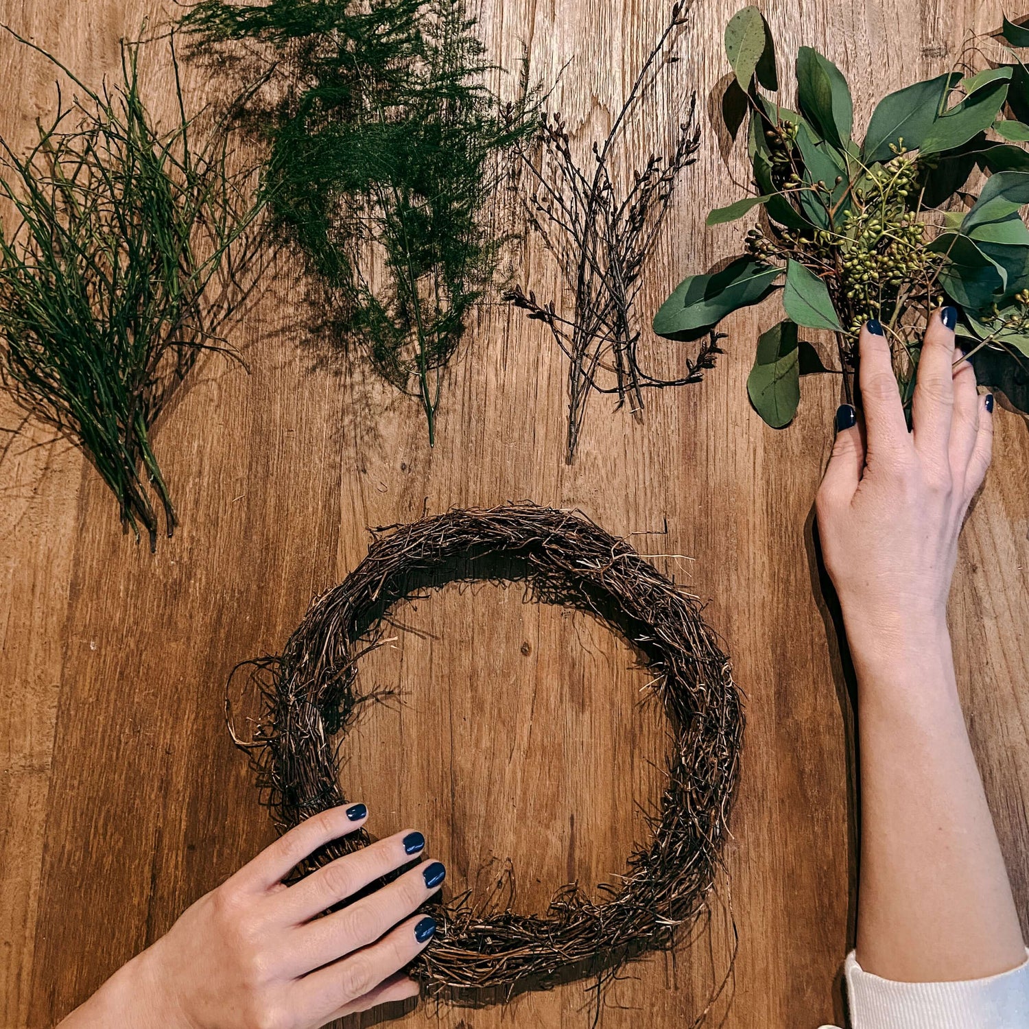 Hände halten geformte Zweige in Ringform mit grünen Blättern – DIY Kranz für Teamevent.