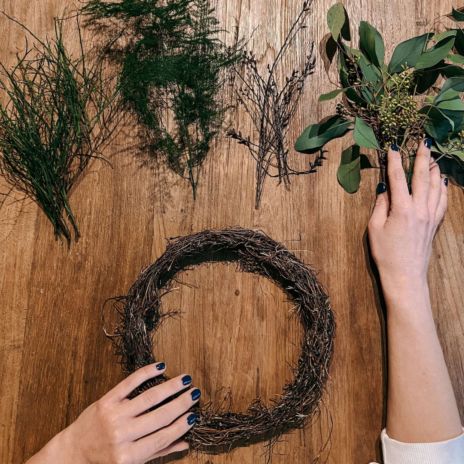 Hände halten geformte Zweige in Ringform mit grünen Blättern – DIY Kranz für Teamevent.