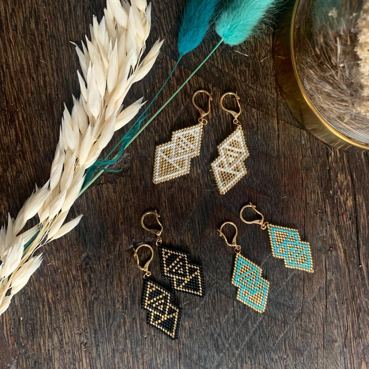 Bunte Boho-Ohrhänger in schwarz, blau und weiß mit goldfilled Metall, handgefertigt, dekorativ auf Tisch arrangiert.