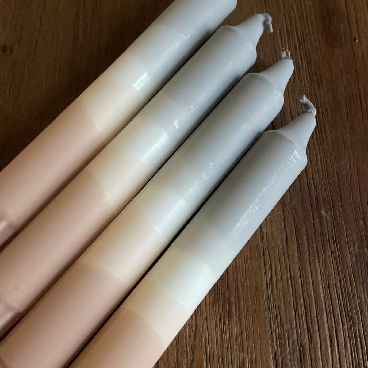 Vier Dip Dye Kerzen „Mountain Dany“ aus Stearin auf Holztisch neben weißem Kerzenständer – handgetauchte Unikate.