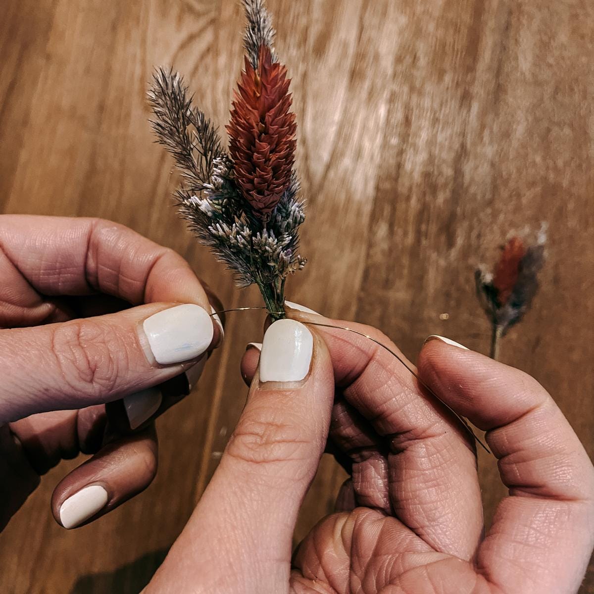 Hände wickeln Draht um Trockenblumen – Bastelschritt der DIY Box Trockenblumenring Lachsflieder.