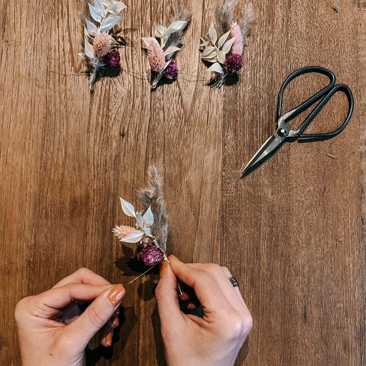 Hände binden kleine Blumen zusammen mit Schere – Vorbereitung für DIY Trockenblumenring.