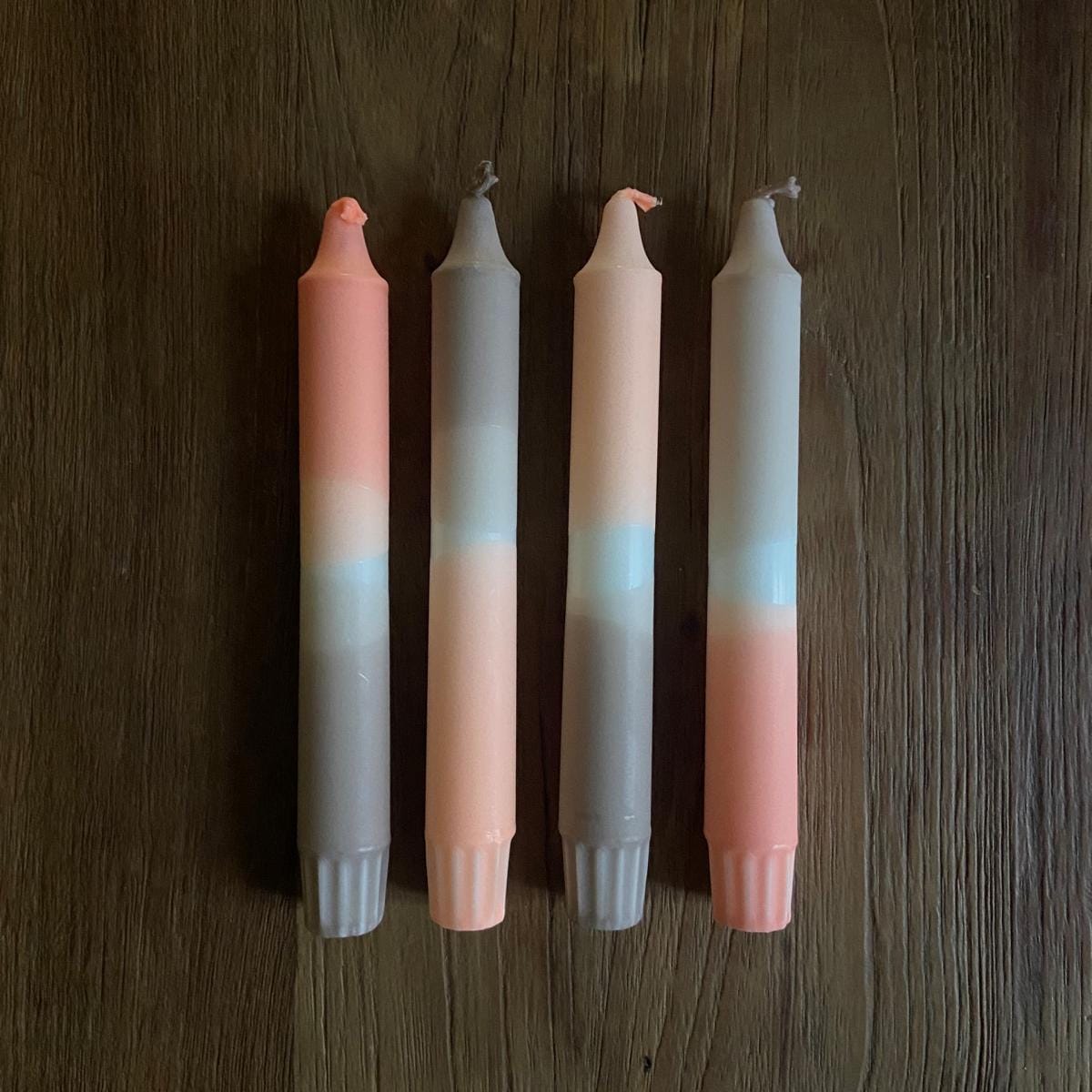 Vier Dip Dye Kerzen „Len“ aus Stearin auf Holztisch neben weißem Kerzenständer – handgetauchte Unikate.