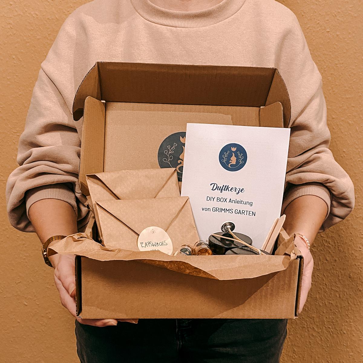 Person hält offene DIY Box mit Materialien für vegane Duftkerzen – kreatives Geschenkset.