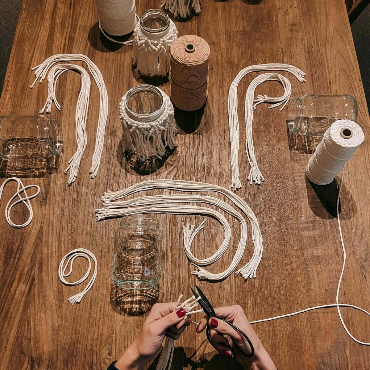 Hand schneidet Garn auf Holztisch – Makramee Workshop für DIY Boho Lichtglas und Dekoration.