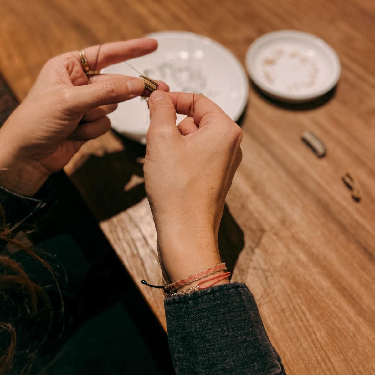 Zwei Hände fädeln verschiedene Ringe auf Draht, Materialien im Hintergrund – DIY Perlenring Workshop