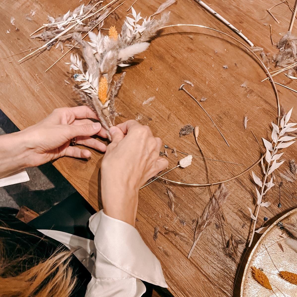 Zwei Hände arbeiten an Ring mit weißen und orangenen Trockenblumen – DIY Boho-Ring Workshop, JGA.