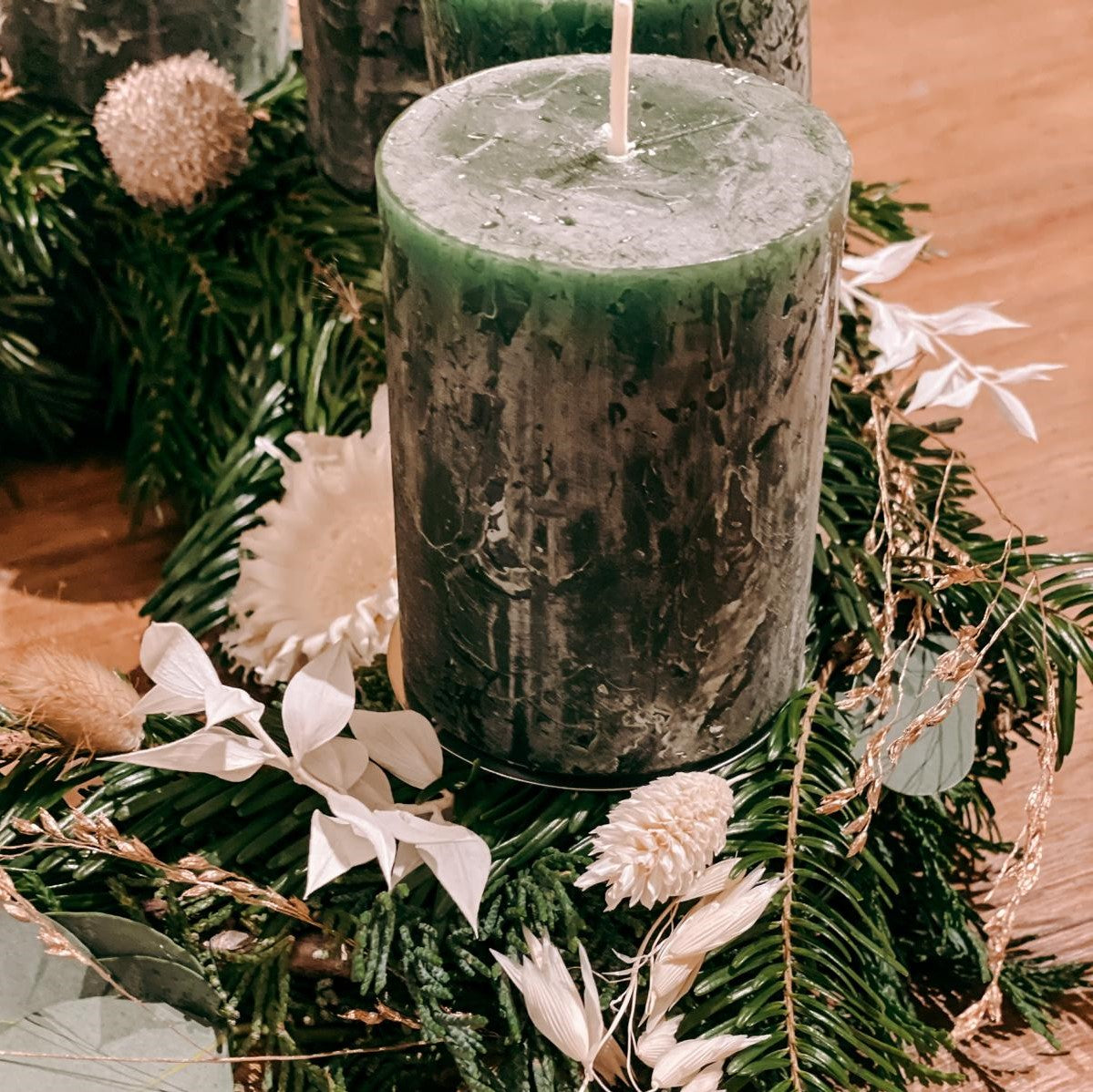 Detailaufnahme einer grünen Kerze mit weißen Blüten – Adventskranz Hänsel in Naturfarben.