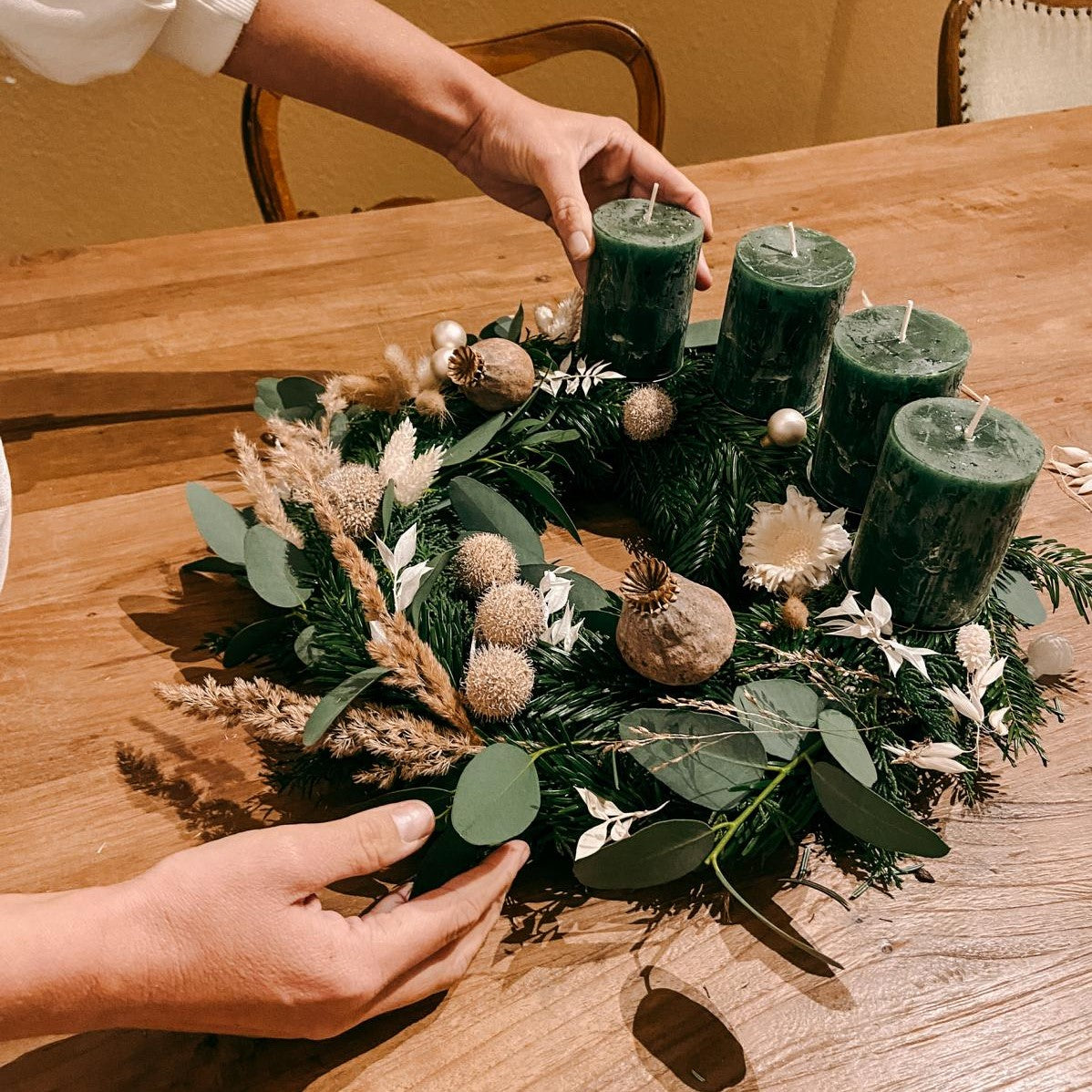 Hand platziert grüne Kerze auf Kranz – Weihnachtskranz selber machen mit DIY Box Hänsel.